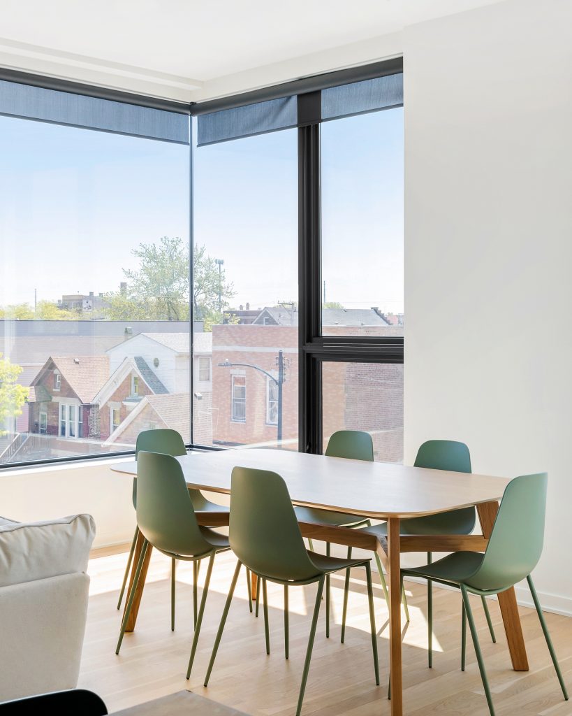 Light and bright dining room with frameless corner window. Modern dining room table with green plastic molded chairs.