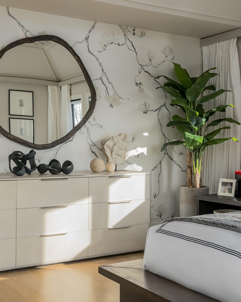 Light splashing along a modern white dresser in a bedroom with bold wallpaper and a statement mirror.