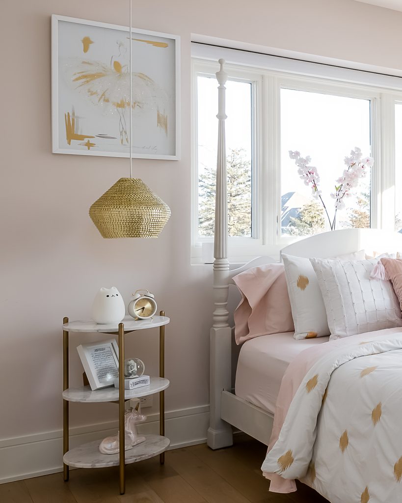 Styled bedside table in pink feminine room with gold accents and lighting.