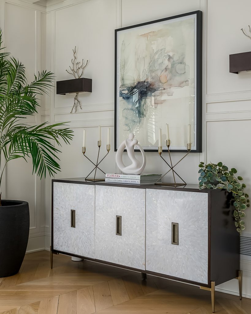 Styled sideboard in modern living room with candles, modern art, and large plant.