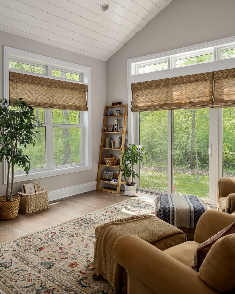 A rustic sitting room with floor to ceiling windows and views of the woods.