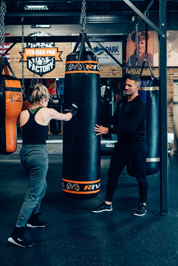 Personal trainer supervising client hitting punching bag