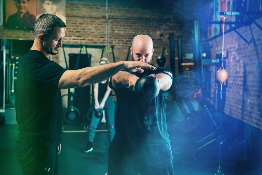 Personal trainer supervising client using kettle bell